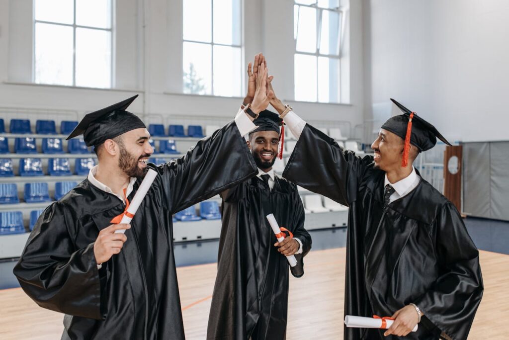 pexels-photo-7942542 Three graduates in gowns celebrating their success with high fives indoors.