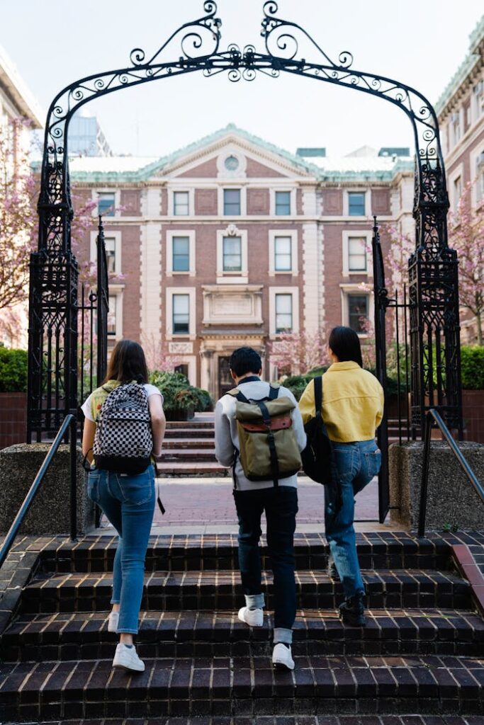 A group of students with backpacks walks towards a university building through an arch.